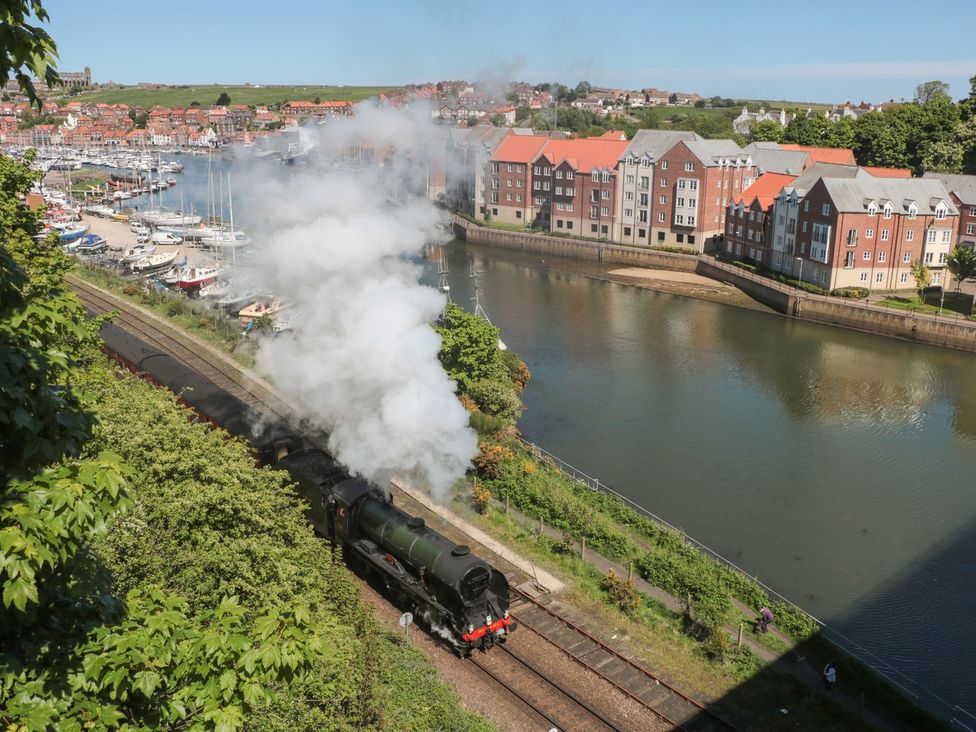 A train emitting smoke near a river with houses at The Shipwrights Whitby