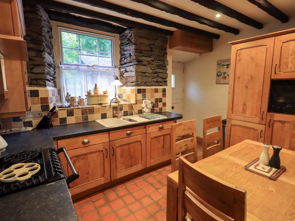 A kitchen with wooden cabinets and a dining table at Stoker’s Cottage in Windermere