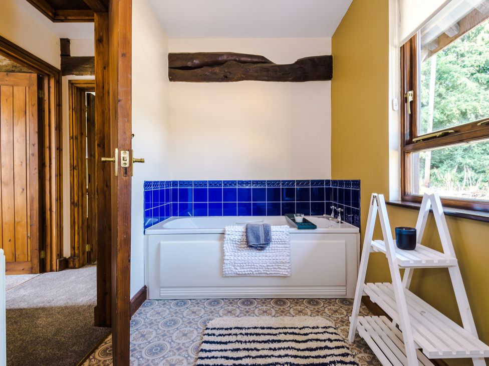 A bathroom featuring a bathtub with blue tiles and a white shelf at Idris Barn Dolgellau