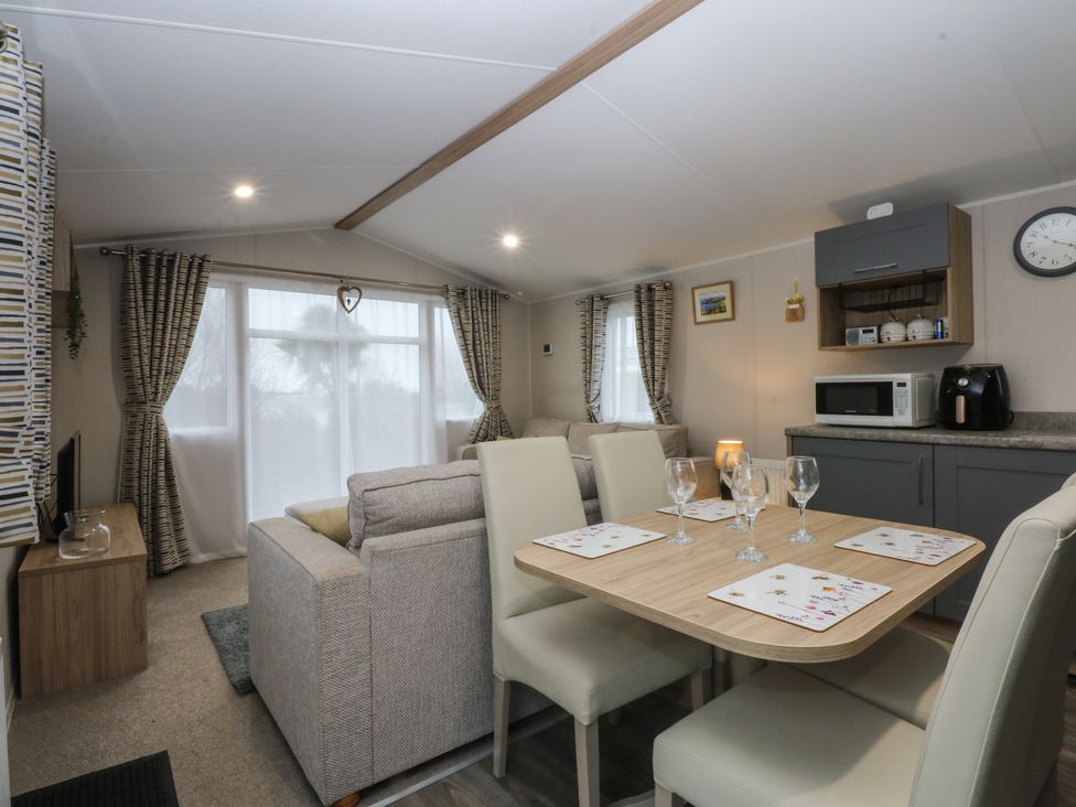 A living room with a dining area and kitchen appliances at Woodland Way in Benllech