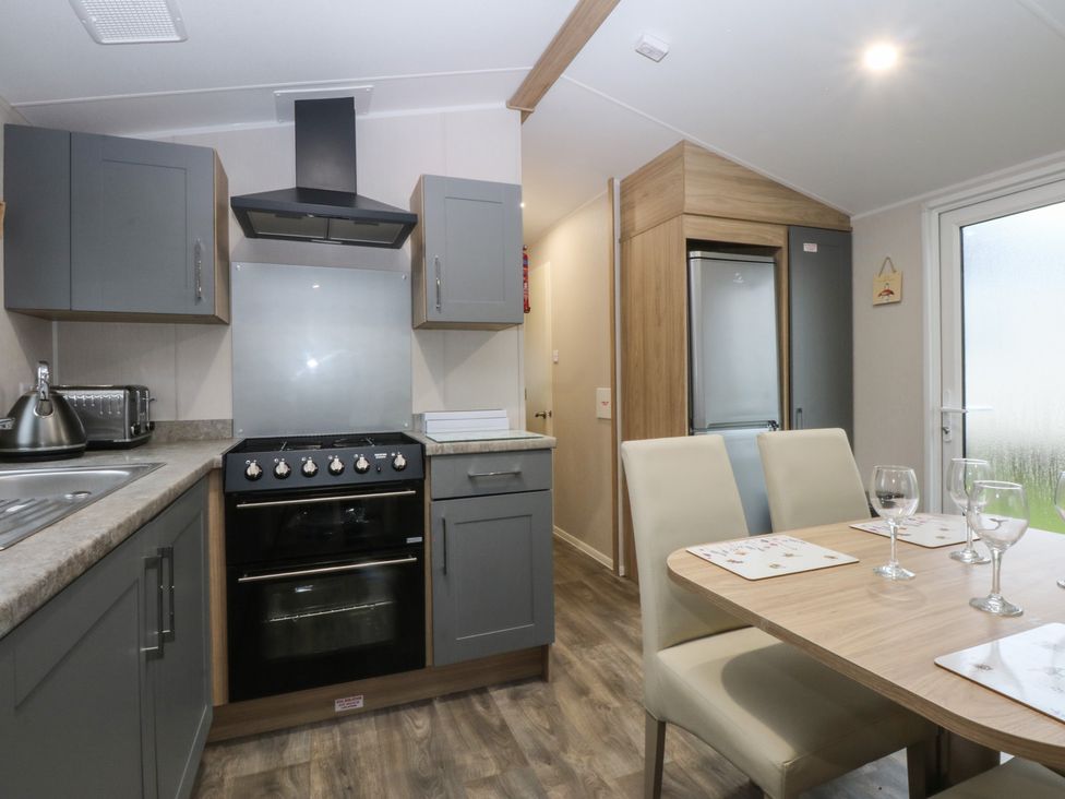 A kitchen with appliances and dining table at Woodland Way in Benllech