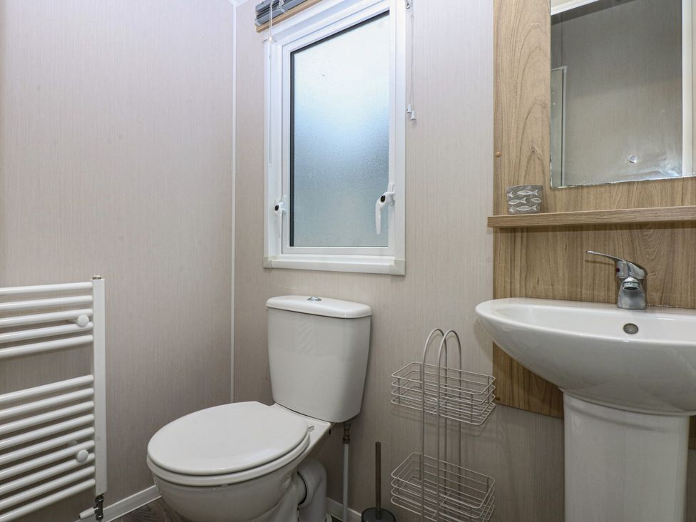 A bathroom with a toilet, sink and window at Woodland Way in Benllech