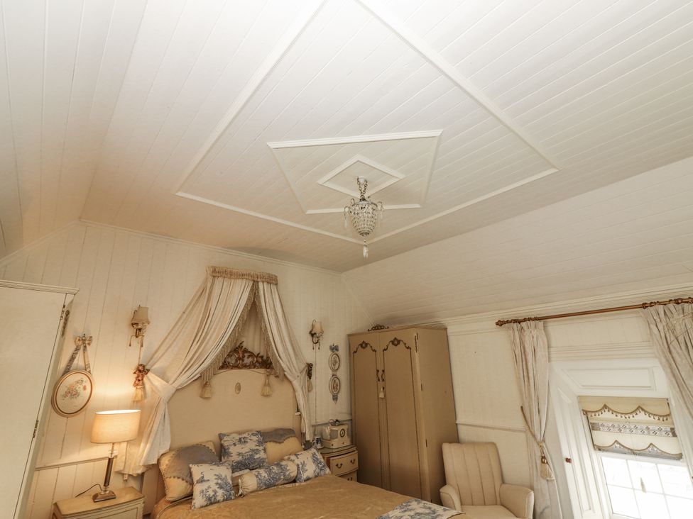 A bedroom with a bed, nightstand, wardrobe, and armchair at White Heather Cottage in Killalou