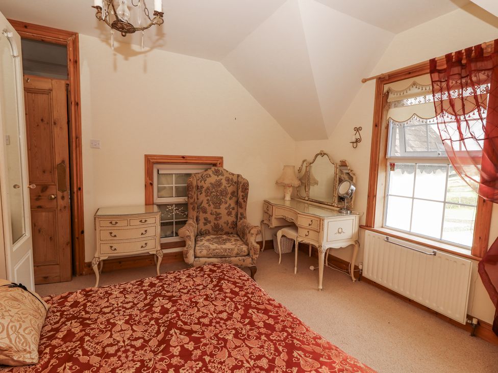A bedroom with a bed, armchair, and vanity table at White Heather Cottage in Killalou