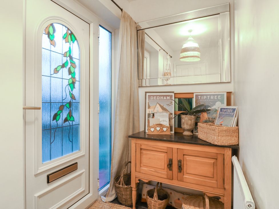 A hallway with a front door and a table displaying baskets and magazines at Berkley Cottage in Colchester