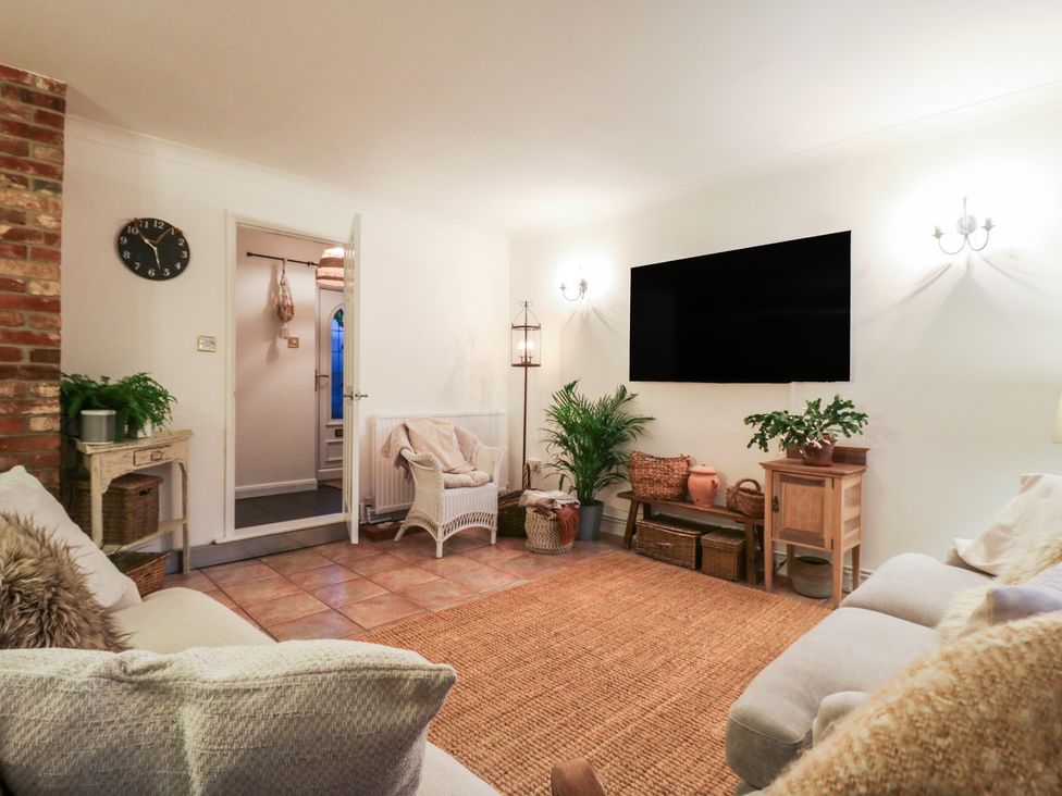 A living room with a clock, television, and plants at Berkley Cottage in Colchester