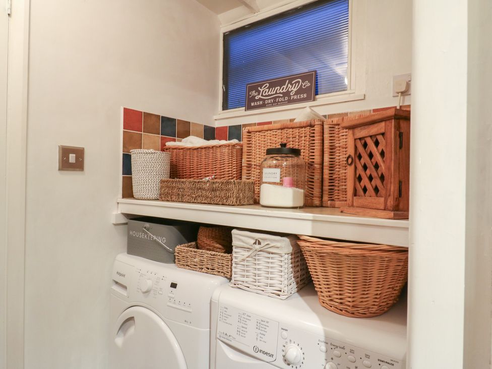 A laundry room with washing machine and storage baskets at Berkley Cottage in Colchester