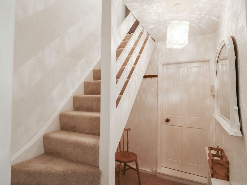 A hallway with stairs, a chair, and a mirror at Berkley Cottage in Colchester