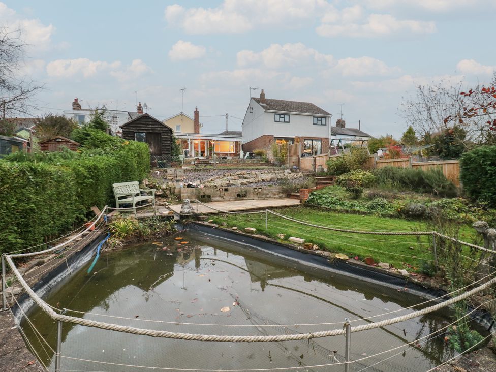 A garden with a pond and benches at Berkley Cottage in Colchester