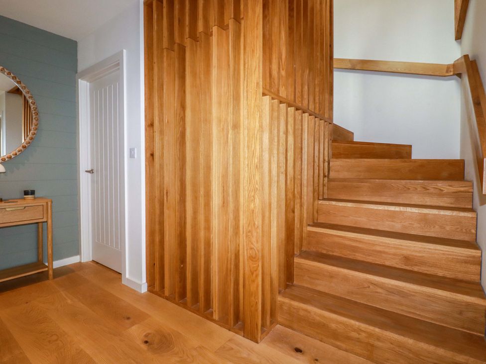 A hallway with wooden stairs and a wall mirror at 8 Karn Havos St. Eval near Mawgan Porth