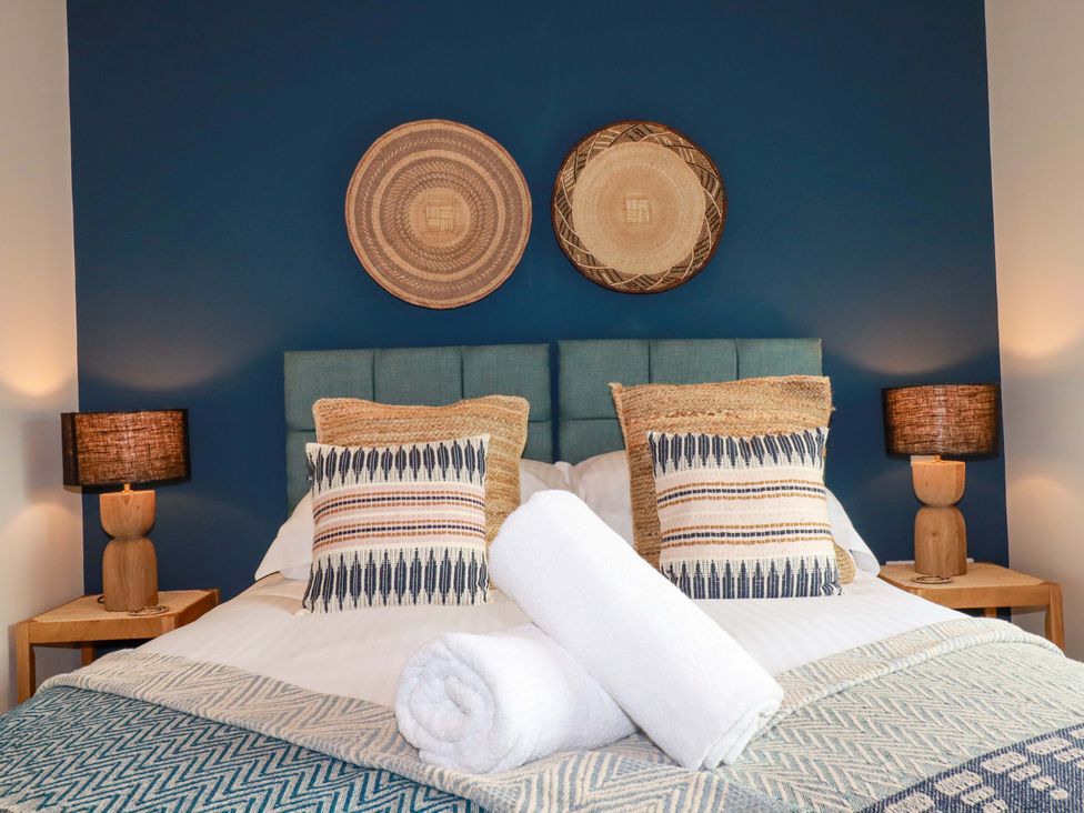 A bedroom with a blue wall and decorative pillows at 8 Karn Havos in St. Eval near Mawgan Porth