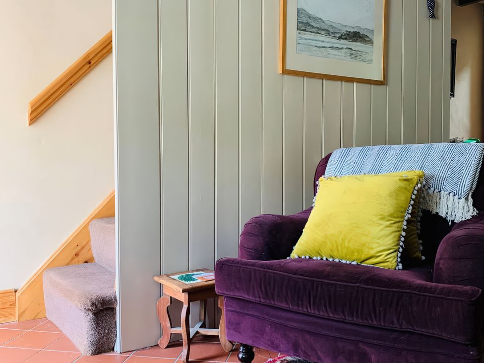 A living room with an armchair and staircase at Copper Miners Cottage, Beddgelert, Eryri (snowdonia)