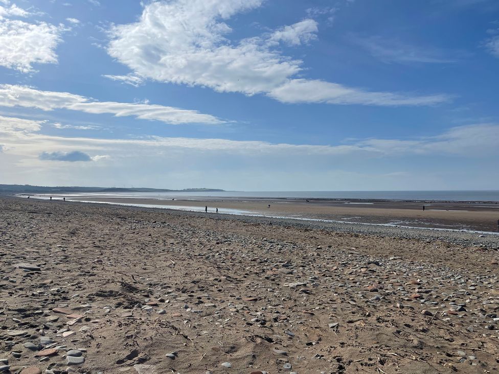 A beach with people walking along the shoreline at Sun House in Allonby