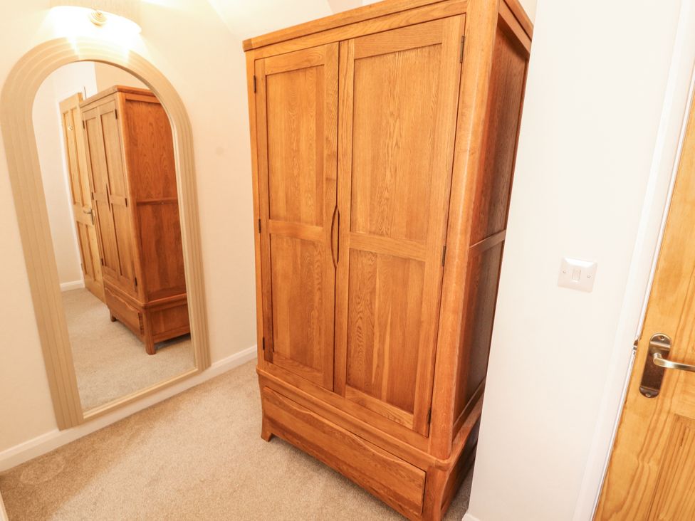 A bedroom with a wooden wardrobe and mirror at Sun House in Allonby