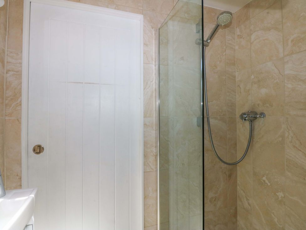 A shower area with a glass door and a white door at Swn Y Don