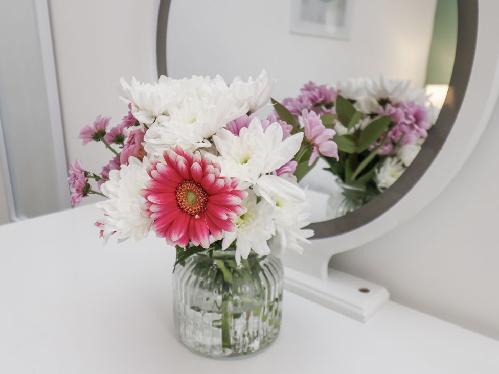 A vase of flowers on a table with a mirror at Apartment 2 in Redcar