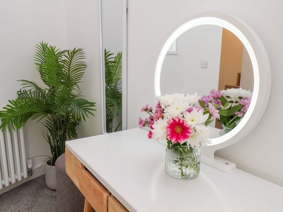 A table with a mirror and flowers beside a plant at Apartment 1 ( 2 bed ) Redcar