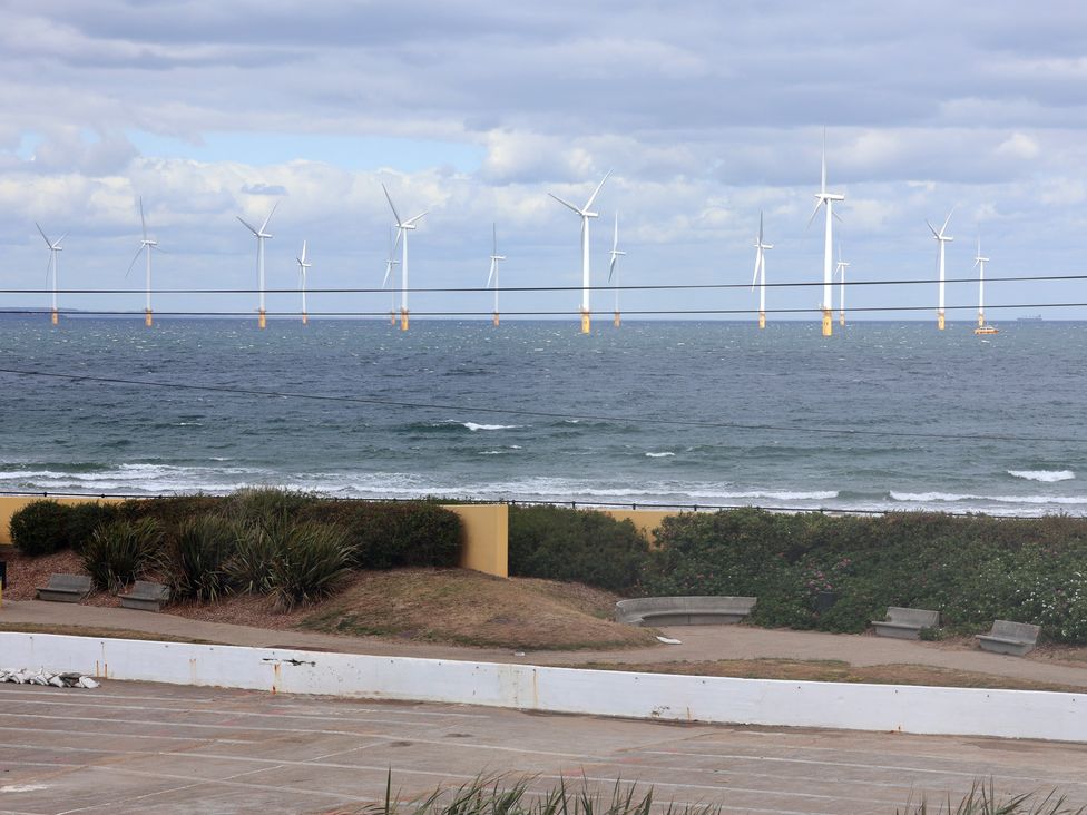 An ocean view with wind turbines and benches at the coastline