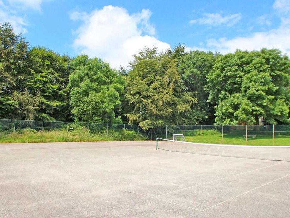 A tennis court with a net and trees at Valley Lodge 2 in Callington