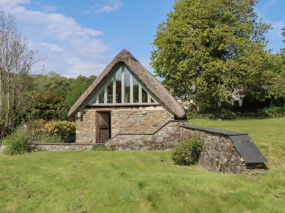 A house with a thatched roof and stone walls at Lower Velwell Barn in Totnes