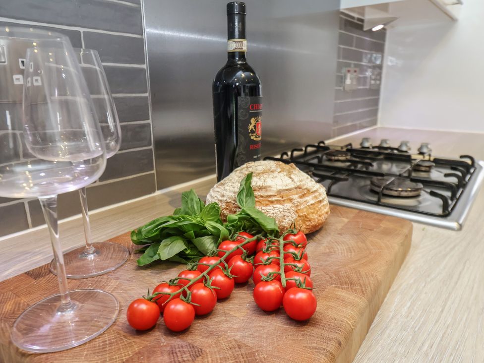 A kitchen with a wine bottle, glasses, tomatoes, basil, and bread at Pearl Stone House in Whitby