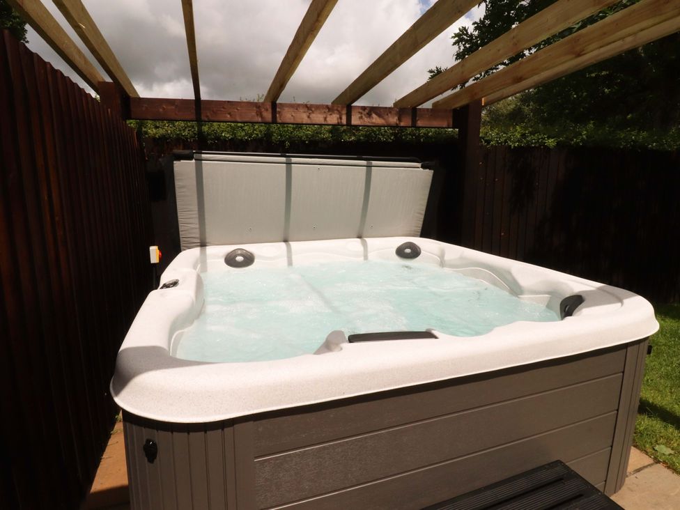A hot tub with water under a wooden pergola in the garden at Heron View