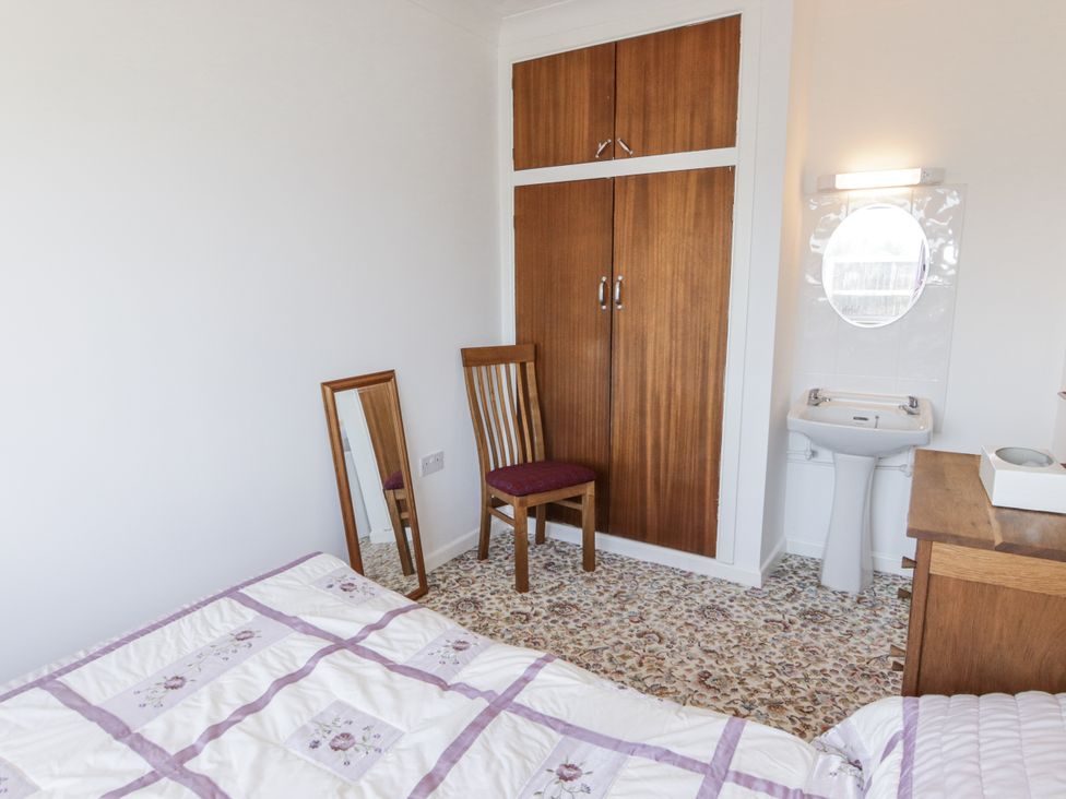 A bedroom with a bed, chair, mirror, wardrobe, and sink at No.1 Vanderhoof Way in Saundersfoot