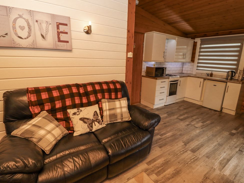 A living room with a sofa and kitchen area at Farnes Lodge Longframlington
