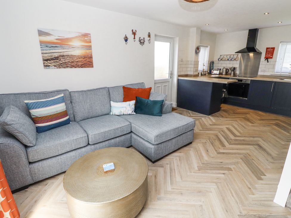 A living room with a sofa and kitchen area at Seahorse Cottage in Chathill