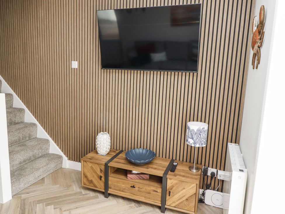 A living room with a television and wooden furniture at Seahorse Cottage in Chathill