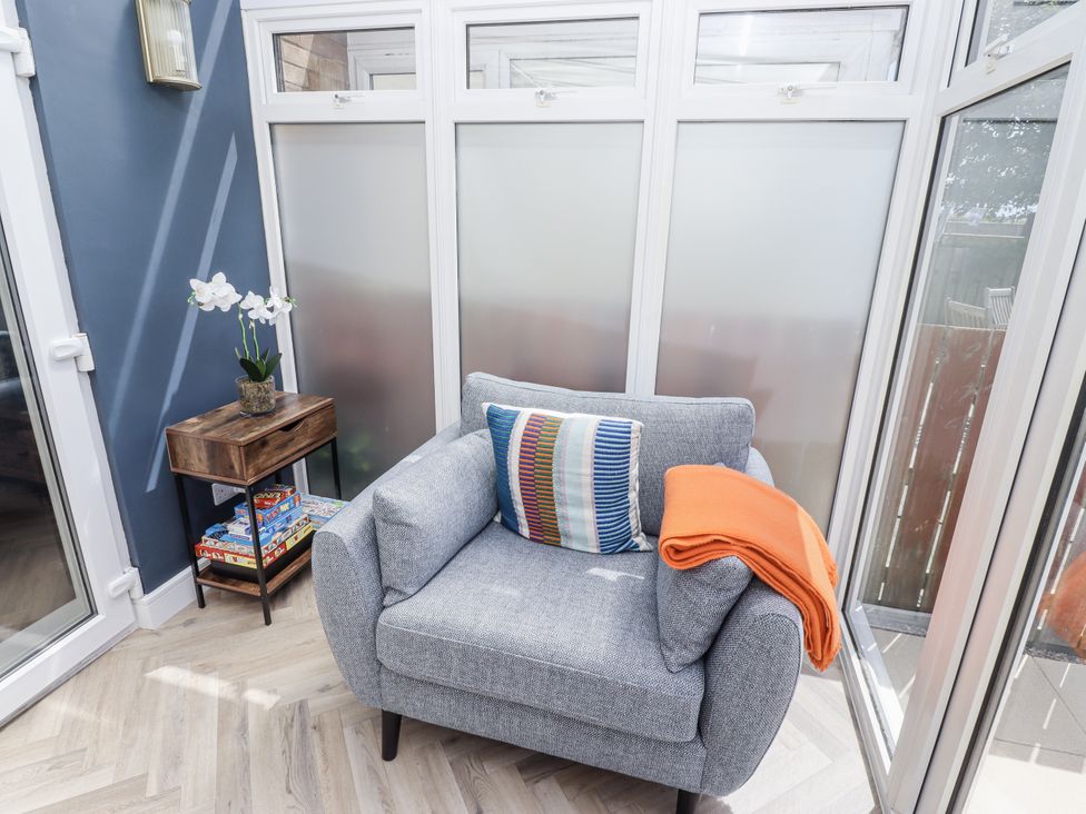 A conservatory with an armchair and side table at Seahorse Cottage in Chathill