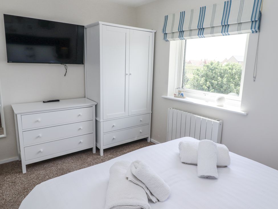 A bedroom with a television, wardrobe, and chest of drawers at Seahorse Cottage in Chathill
