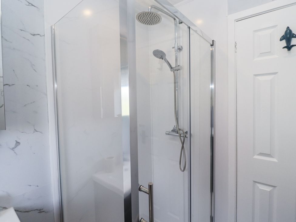 A shower enclosure with a glass door and showerhead at Seahorse Cottage in Chathill