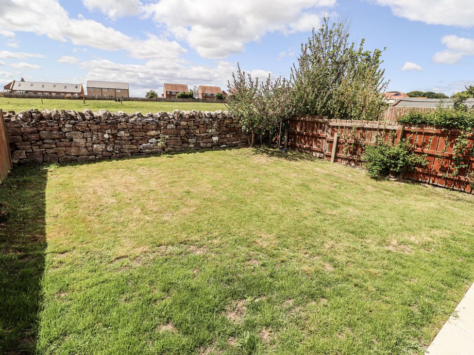 A garden with grass and a stone wall at Seahorse Cottage in Chathill
