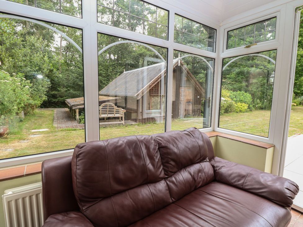 A conservatory with a sofa and windows overlooking the garden at The Anchorage in Hoveton & Wroxham