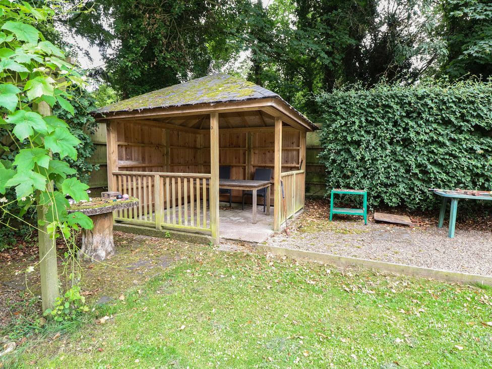 A wooden gazebo with a table and chair in a garden at The Anchorage Hoveton & Wroxham