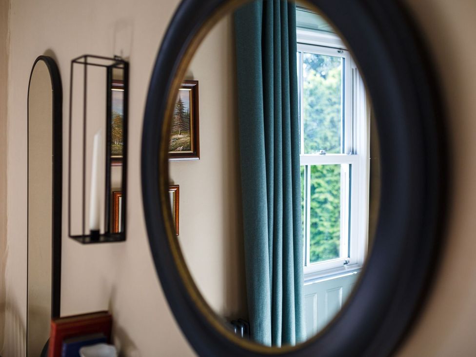 A mirror reflecting a window with curtains and framed pictures at Grove House in Grange-Over-Sands