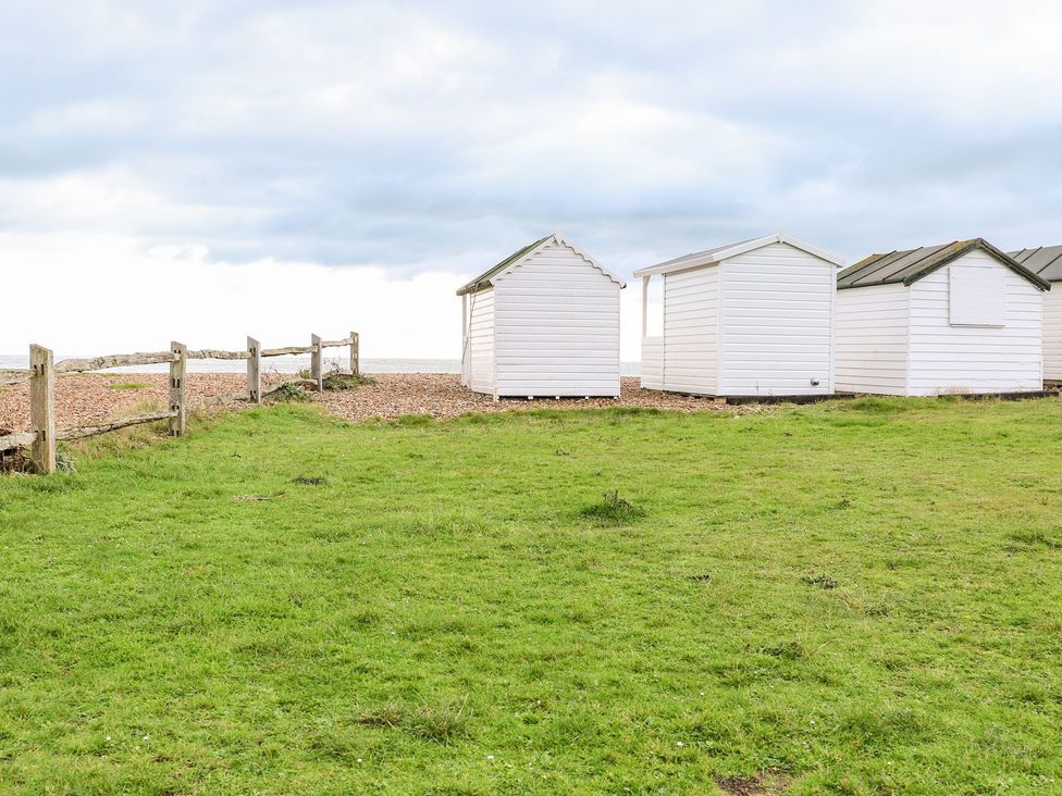 Beach huts alongside a fence in a grassy area at 3 Seaview Cottages, Normans Bay near Bexhill-on-Sea