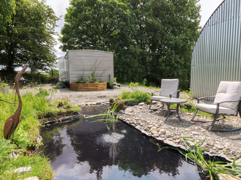 An outdoor area with a pond, chairs and a shed at Gwybedog in Llanwrda
