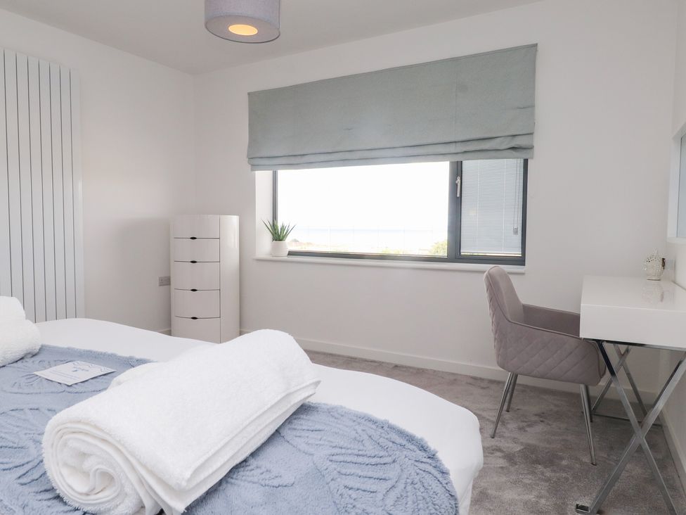 A bedroom with a bed, desk, and storage unit at Môr Glas in Deganwy