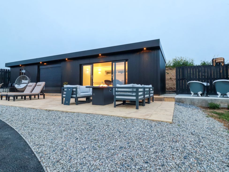 An outdoor seating area with a table and hot tubs at The Lake Boat exclusive retreat Black Cross near St Columb Major