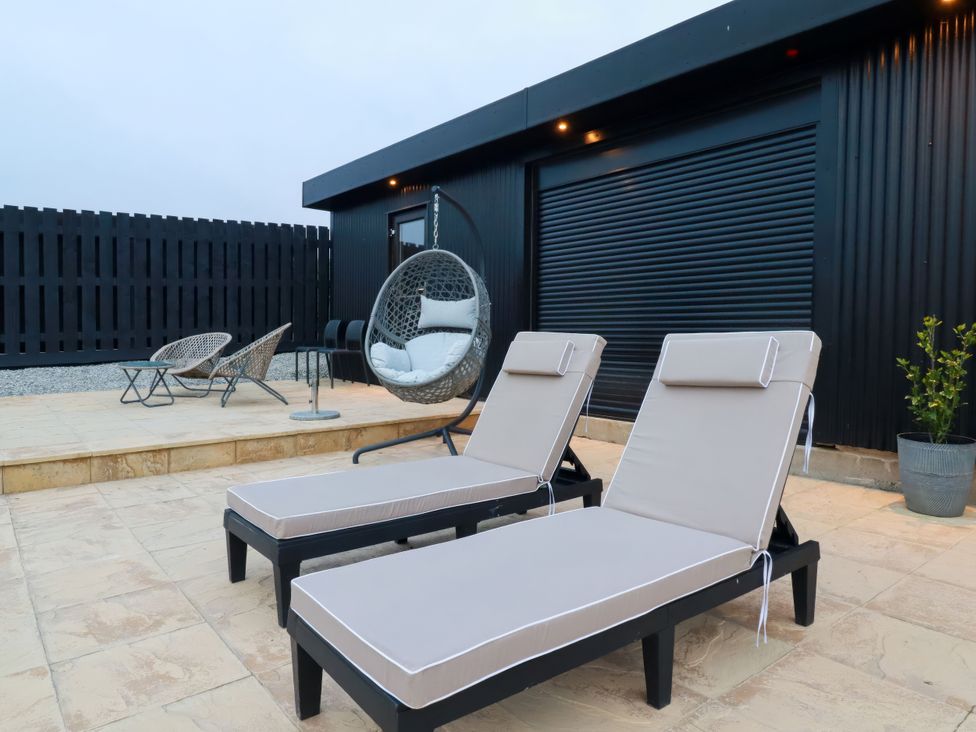 Outdoor seating area with lounge chairs and a hanging chair at The Lake Boat exclusive retreat Black Cross near St Columb Major