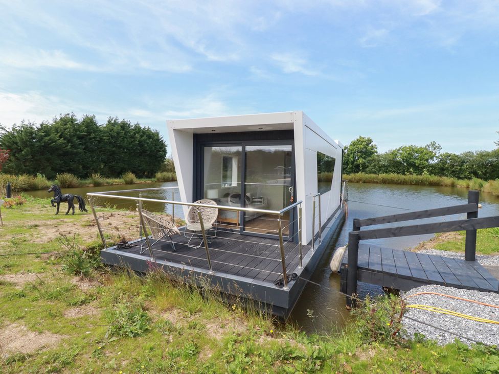A boat on water with a wooden deck and railing at The Lake Boat exclusive retreat Black Cross near St Columb Major