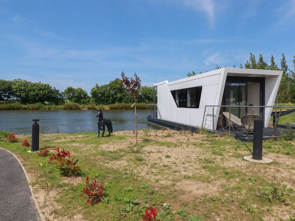 A houseboat by the water with a statue and plants at The Lake Boat exclusive retreat Black Cross near St Columb Major