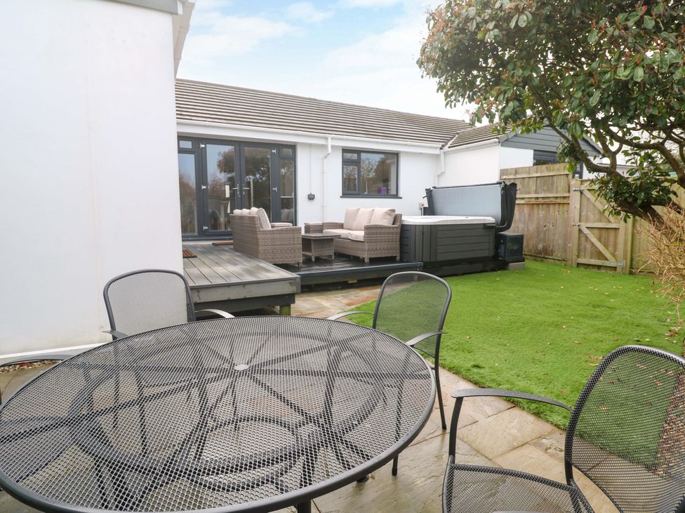 A garden with a table and chairs and a hot tub at Byron’s Retreat Crantock