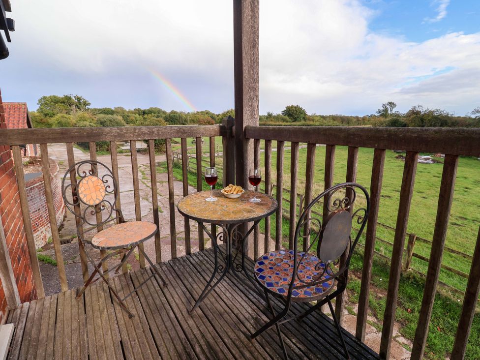 A balcony with a table and chairs overlooking a field at Hayloft in Ipswich