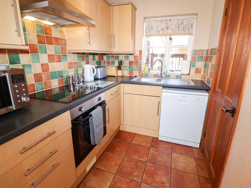 A kitchen with cabinets, sink, appliances and tiled walls at Coachman's Cottage in Ipswich