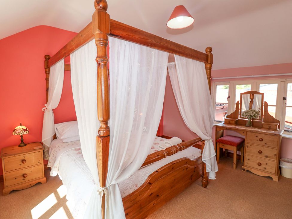A bedroom with a four-poster bed and a dressing table at Coachman's Cottage in Ipswich
