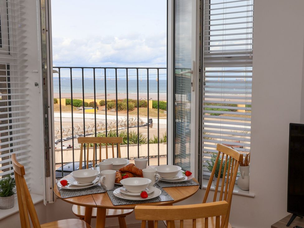 A dining room with a table set near a window overlooking the sea at Apartment 3 (2 bed) in Redcar