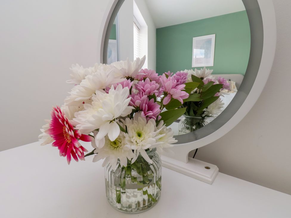 A vase of flowers on a table with a mirror in a bedroom at Apartment 5 (1 bed) Redcar